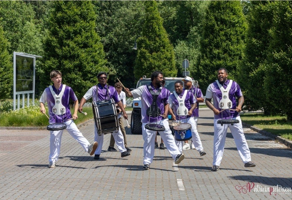 All In 1 Music Brassband in paarse outfits terwijl ze vol energie optredens op een plein