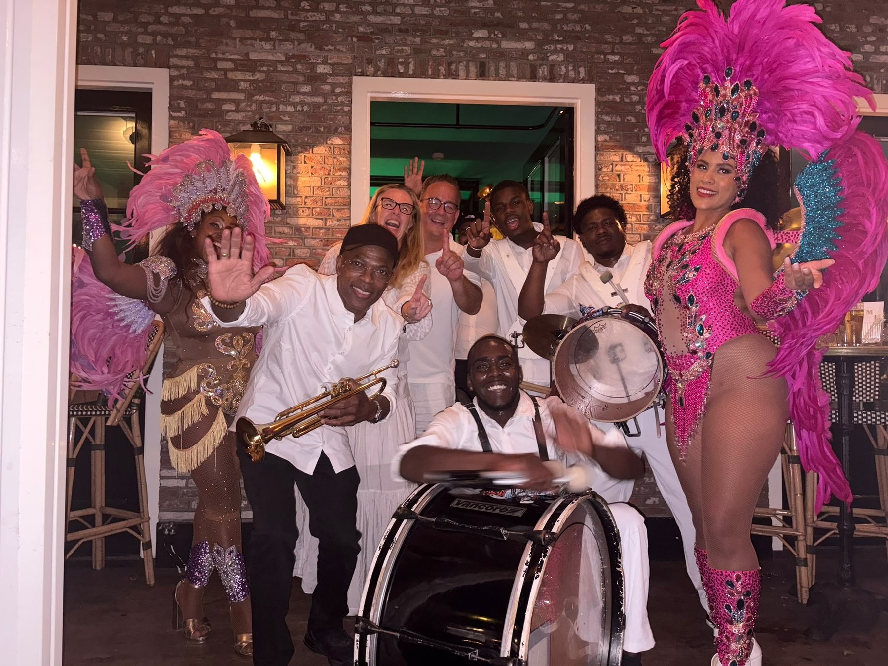 All In 1 band in het wit met twee danseressen in roze verenkostuum tijdens een avondfeest